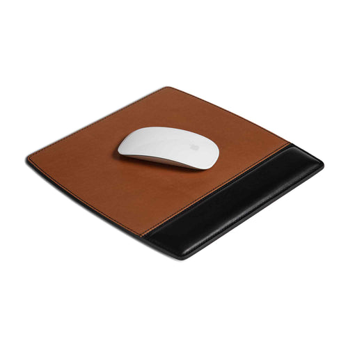 Bumpy Leather Mouse Pad in Maui Taba Brown laid flat at an angle on a white surface with a white Apple Magic Mouse resting on the suede upper panel. Two-tone construction clearly visible — warm taba brown suede tracking surface above, deep black smooth leather wrist rest panel below — with dark contrast saddle stitching along all edges. The raised wrist rest panel shows subtle depth and structure from the side angle.