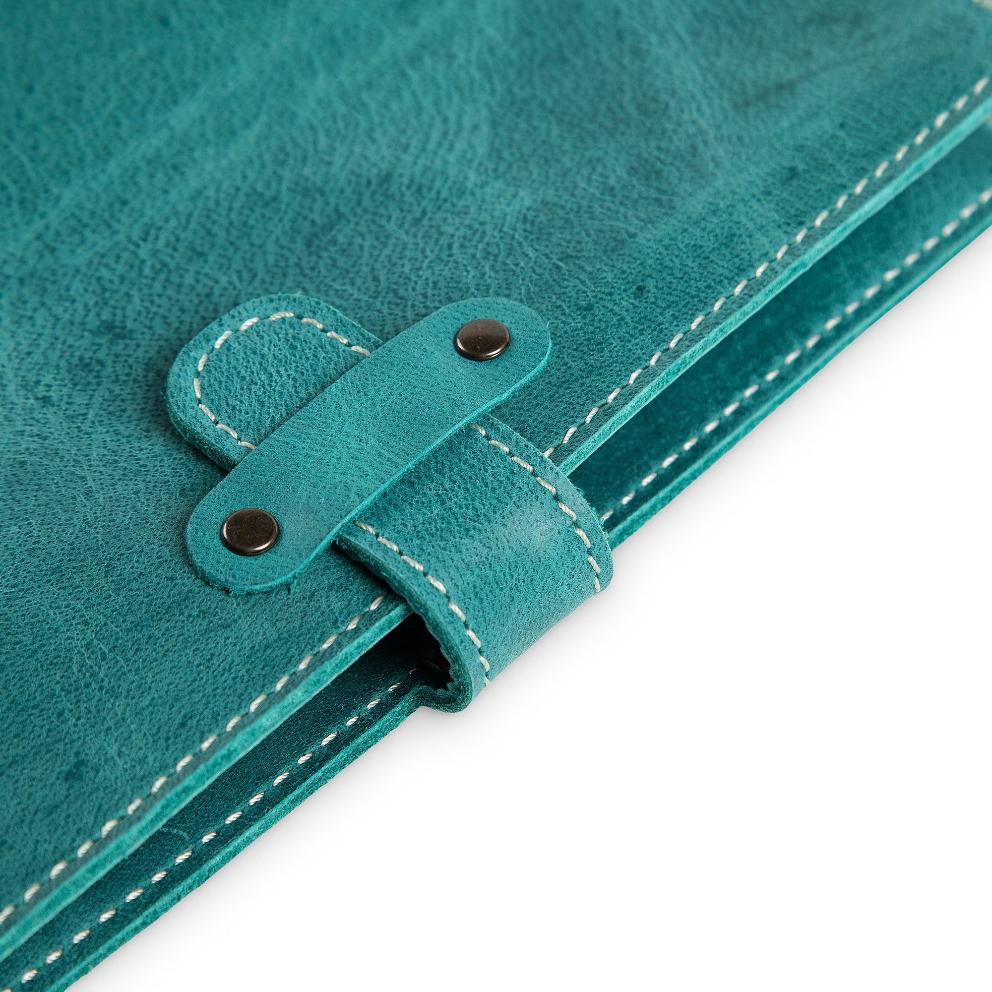 Close-up of DuPage Turquoise Green journal's leather strap closure on Laodamas buffalo leather, showing two antique brass rivets, saddle-stitched strap loop, and cream edge stitching detail. 