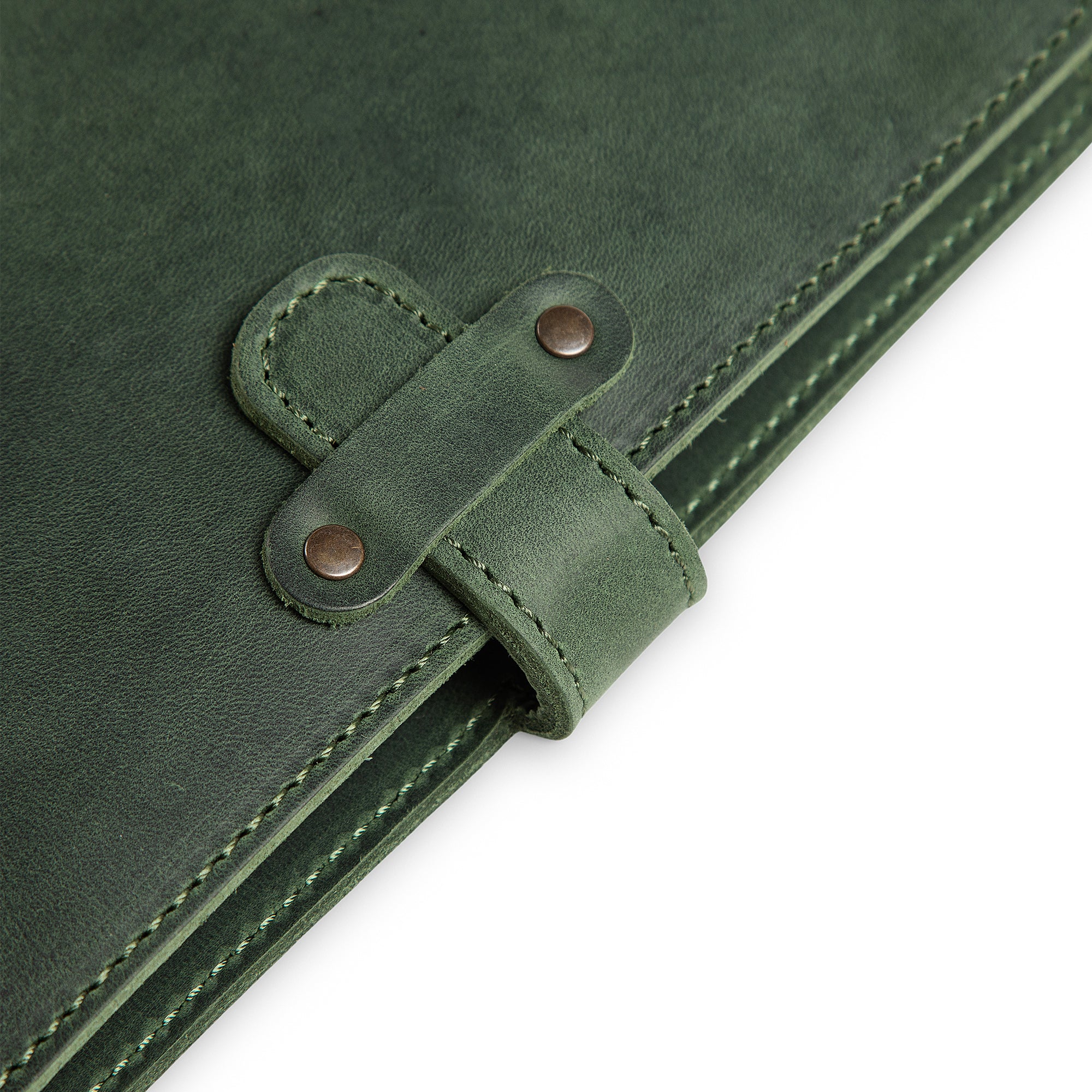 Close-up of DuPage Green journal's leather strap closure on Dallas Crazy Horse surface, showing two antique brass rivets, saddle-stitched strap loop, and green edge stitching detail.
