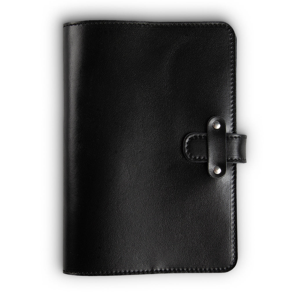 Black Dexios pull-up calfskin leather journal, front cover view, with black saddle stitching along edges and a leather strap closure secured by two silver-tone rivets on the right side.