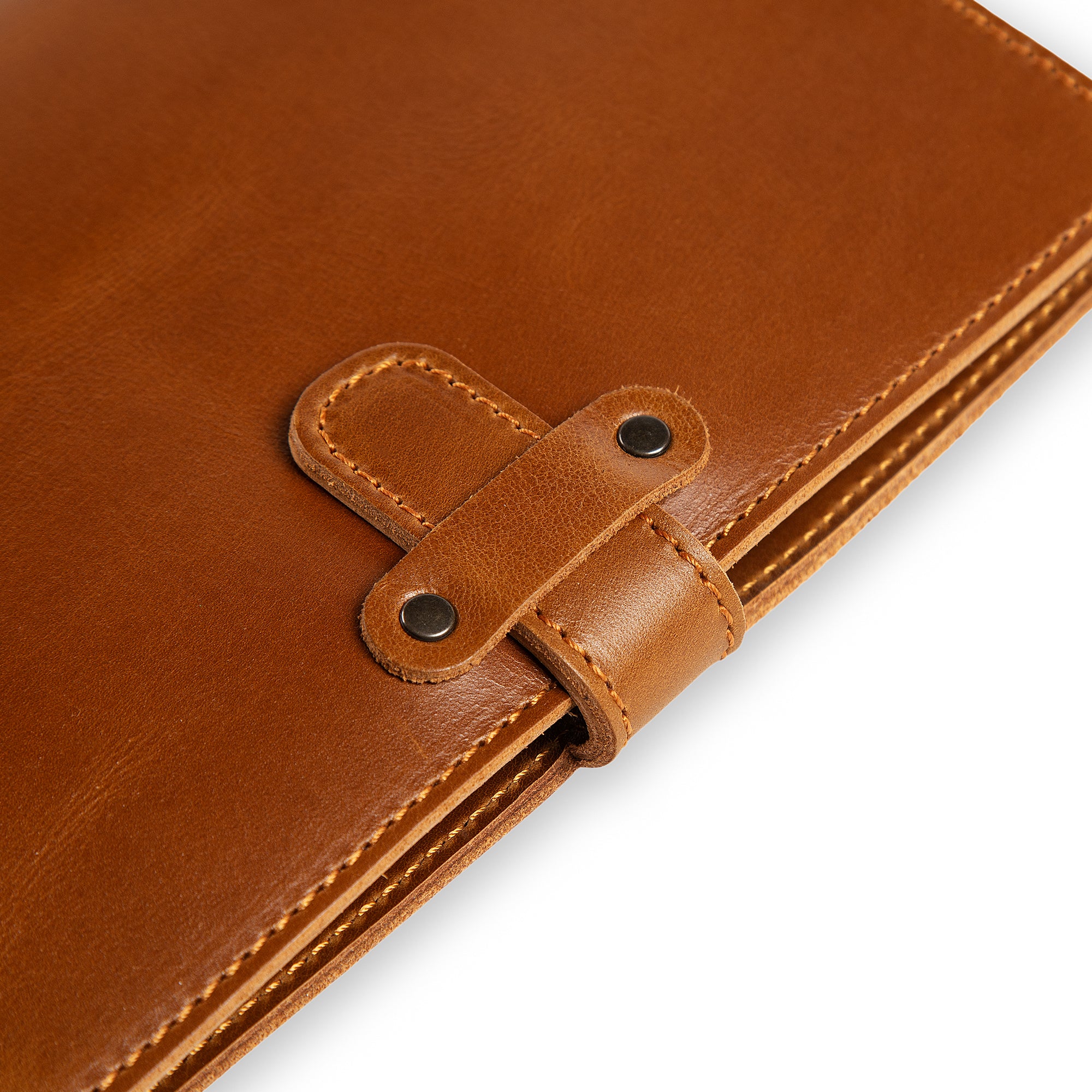 Close-up of DuPage Mustard Brown journal's leather strap closure on Dexios calfskin, showing two antique brass rivets, saddle-stitched strap loop, and orange edge stitching detail.