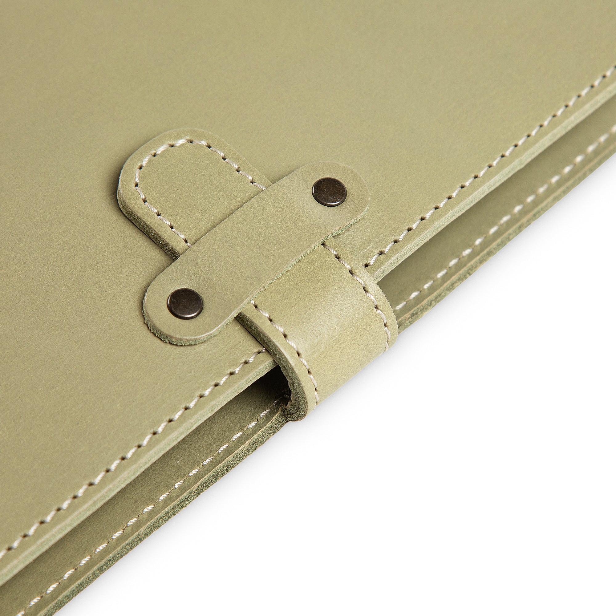 Close-up of DuPage journal's leather strap closure on aqua green Iphitos buffalo leather, showing two antique brass rivets, saddle-stitched strap loop, and cream edge stitching detail.