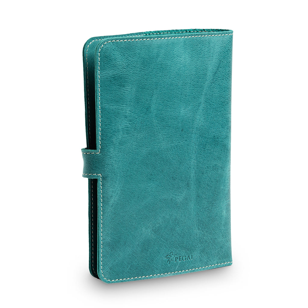 Three-quarter front view of closed turquoise DuPage journal showing spine thickness, cream saddle stitching, side strap closure tab, and embossed PEGAI logo on lower front cover. 