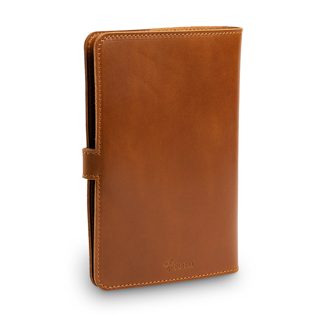Three-quarter angled view of closed mustard brown DuPage leather journal highlighting the leather strap closure with antique brass rivets, orange stitching, and smooth Dexios calfskin surface.
