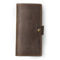 Clark Leather Checkbook Cover in Chestnut Brown, closed and laid flat on a white surface. Dallas Crazy Horse calfskin in a warm deep chestnut tone with natural waxy pull-up surface variation and visible hide markings. Warm tonal saddle stitching runs along all four edges. A small leather tab with an antique brass snap closure sits centered on the right edge.