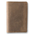 Sand brown crazy horse calfskin passport cover, closed and laid flat. Matte waxy surface in warm taupe with natural tonal variation shifting from pale sand to deeper tan. Hand-stitched edges in matching tan thread. Rounded corners and clean minimal silhouette with no hardware.