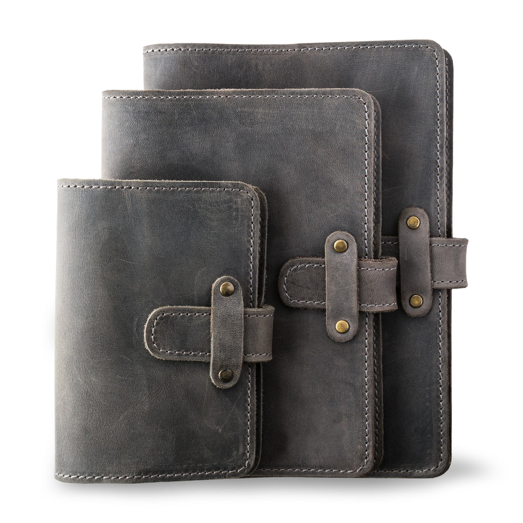 Three DuPage leather journals in rock gray showing Pocket, Midi, and Full size comparison, all with matching gray saddle stitching, antique brass rivets, and heavily distressed cool gray pull-up surfaces. 