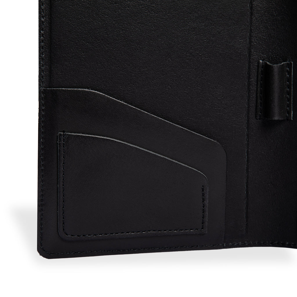 Close-up of PEGAI Eriksen Jr. padfolio interior in charcoal black Iphitos buffalo leather, showing angled business card slot stitching and central pen loop detail. 