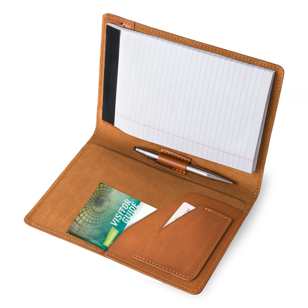 PEGAI Eriksen Jr. padfolio open and in use, holding a lined legal pad, a stylus pen in the center loop, and a visitor guide and cards tucked in the left interior pocket.