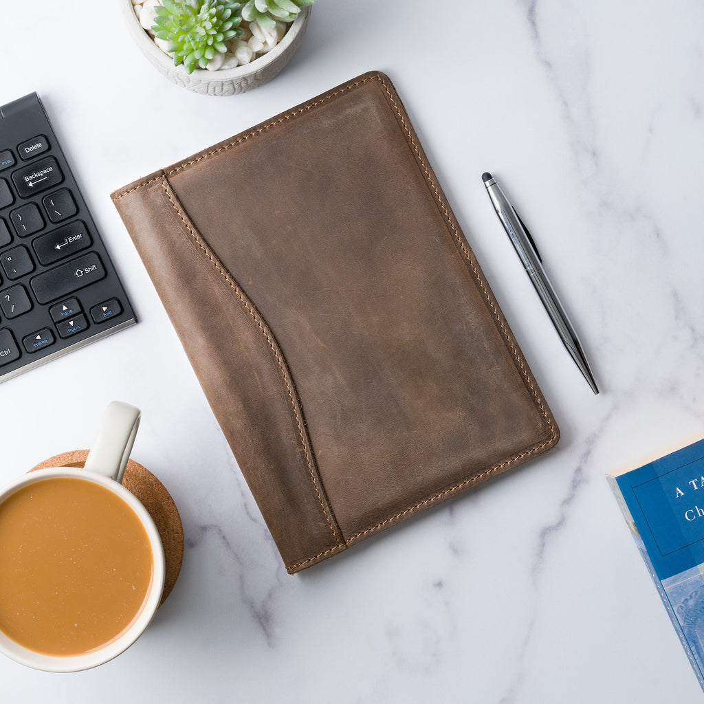 Sand Brown Eriksen padfolio lies flat on a marble desk beside a keyboard, succulent, pen, coffee cup, and book, styled for an office setting.