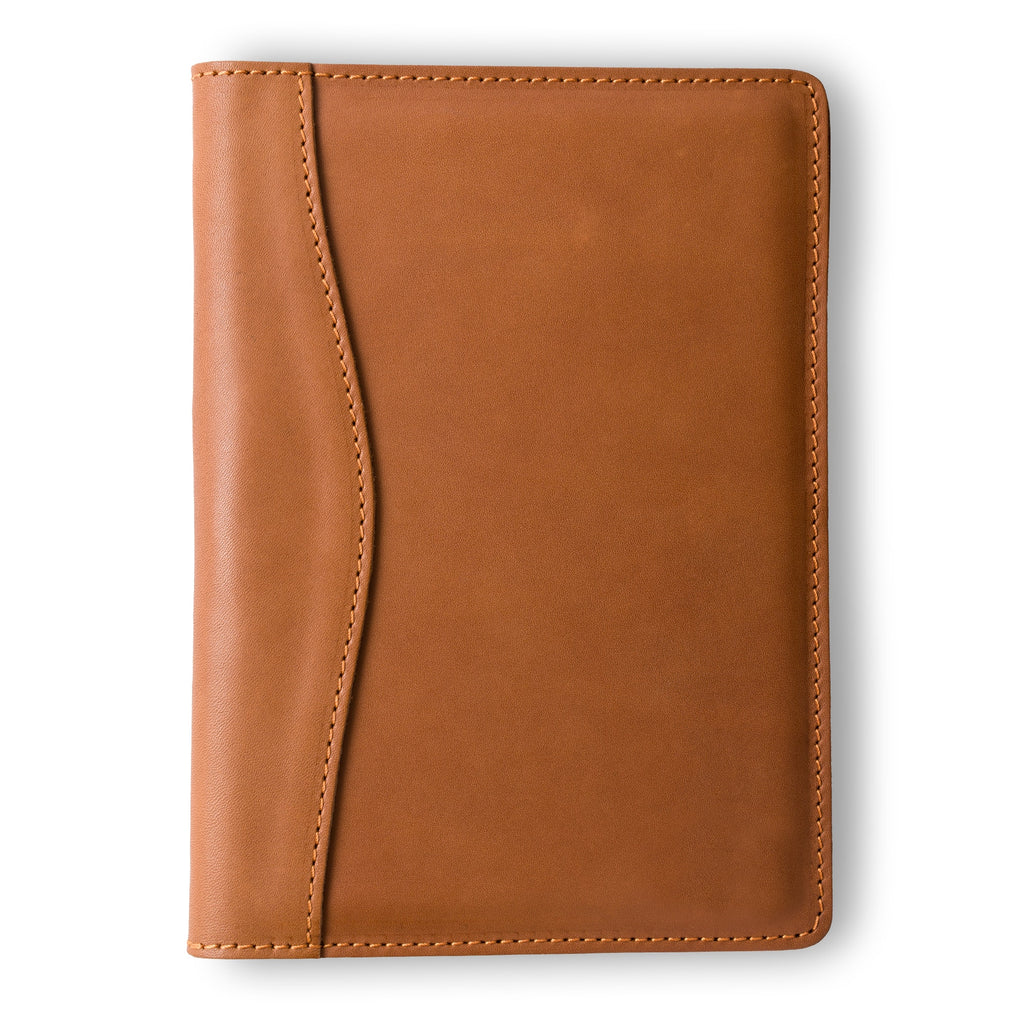 PEGAI Eriksen Jr. padfolio in cognac brown Zurich pull-up calfskin, closed, showing curved seam detail along the spine and natural aniline sheen across the cover. 