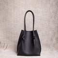 Front view of the Flora Everyday Tote in black Togo leather, showcasing its softly structured silhouette and knotted handle details against a textured neutral backdrop.