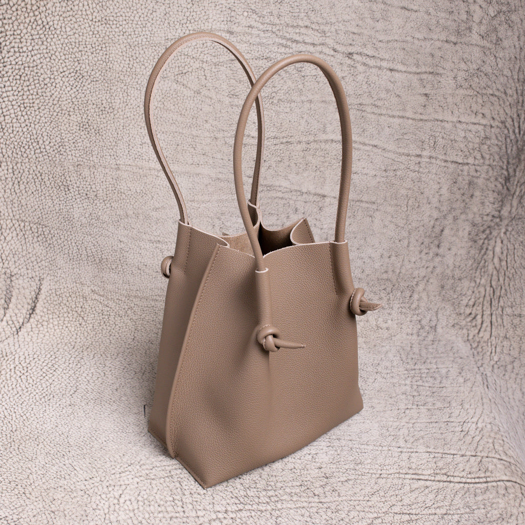 Angled shot of the Flora in Etoupe, highlighting the sculptural shape, upright handles, and folded-edge detailing.