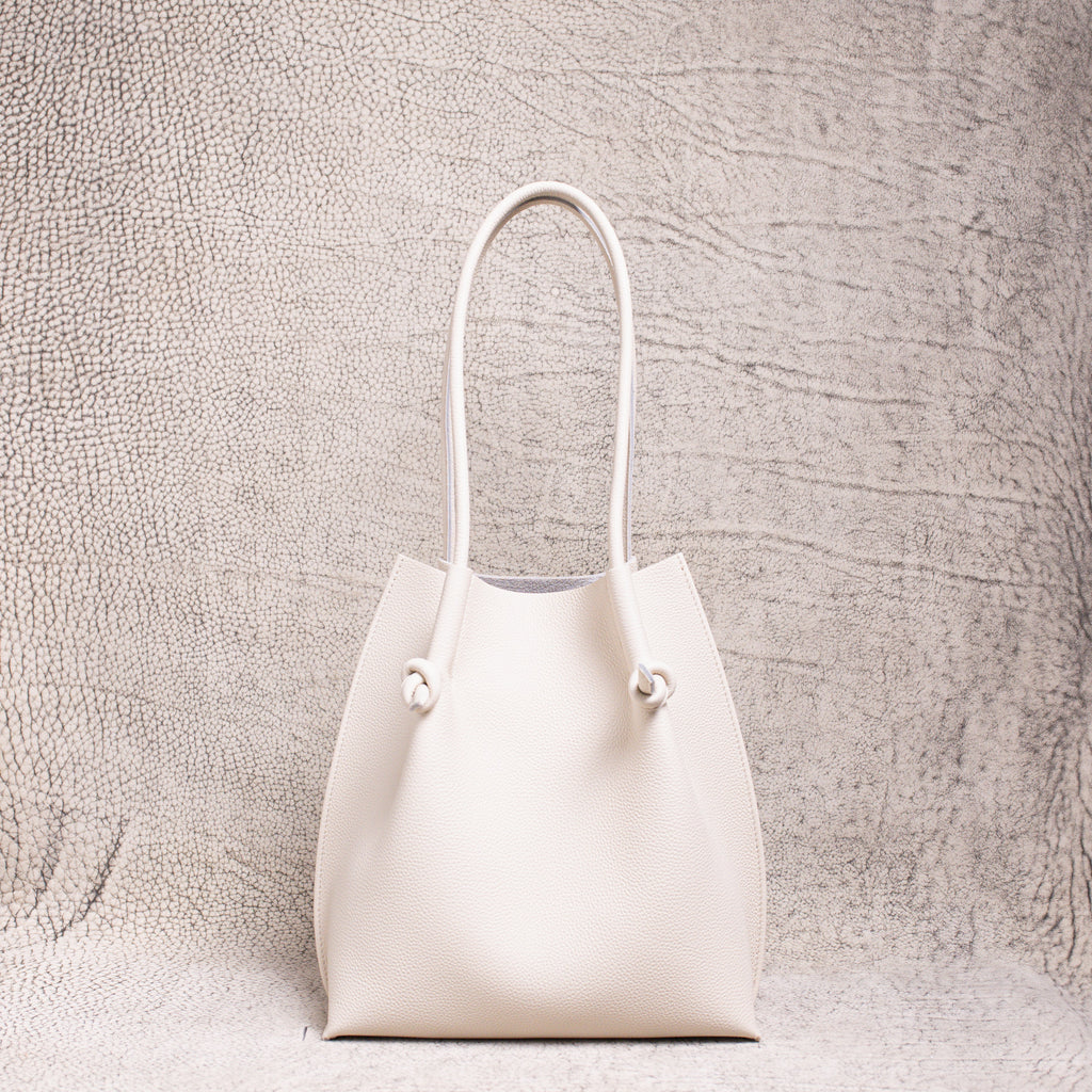 Flora Everyday Tote in Togo Beige leather standing upright on a textured surface.