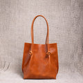 A front-facing view of the Flora Everyday Leather Tote in Dual Tone Whiskey, showcasing its minimalist silhouette and knotted leather handles.