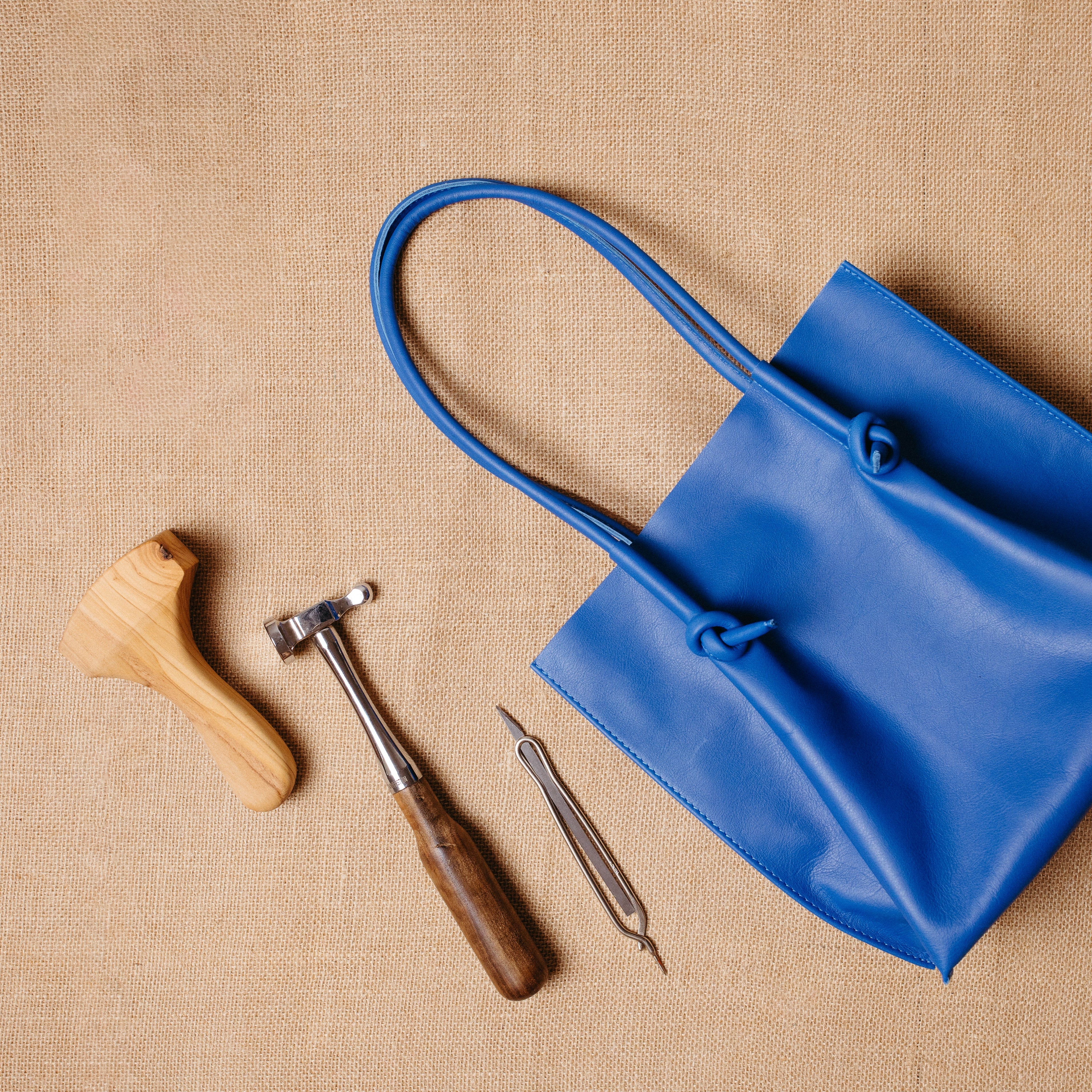 Flat lay of the Flora Leather Tote in blue next to artisan tools, emphasizing its handcrafted quality and Atelier PEGAI’s dedication to traditional leatherwork.
