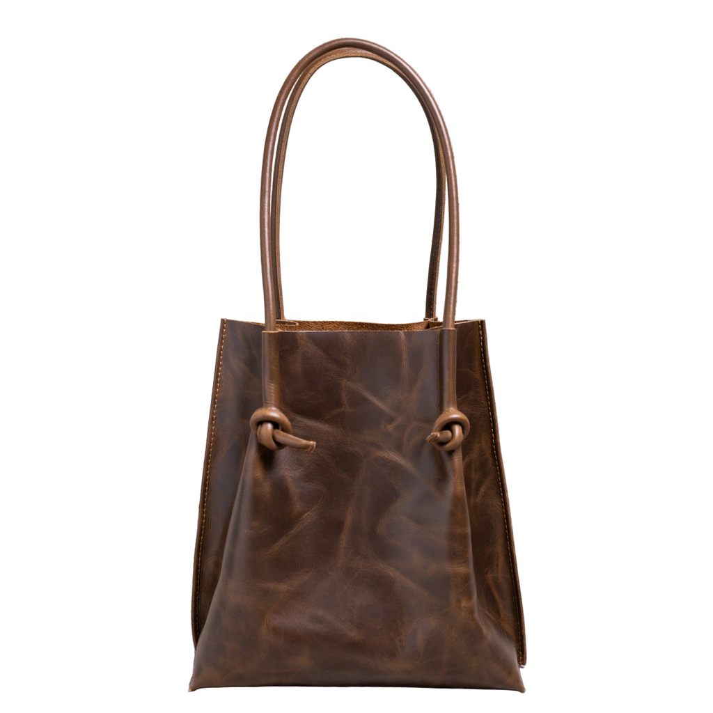 Flora Everyday Tote in Dual Tone Coffee leather stands upright, tall silhouette, with rolled dual handles and a single knotted leather closure on each side of the open top.