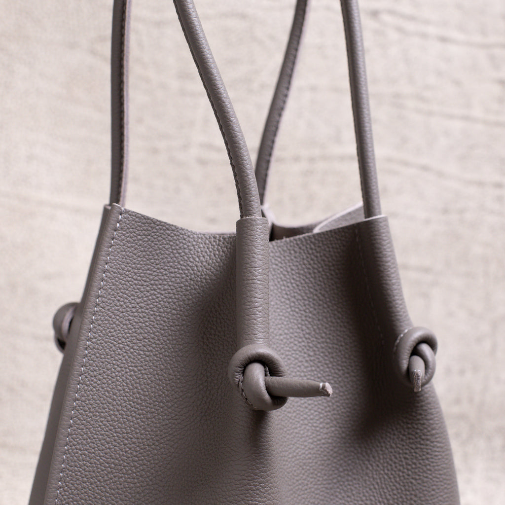 Side angle shot focusing on the dual handles and the tote’s signature knotted construction in gray calfskin.