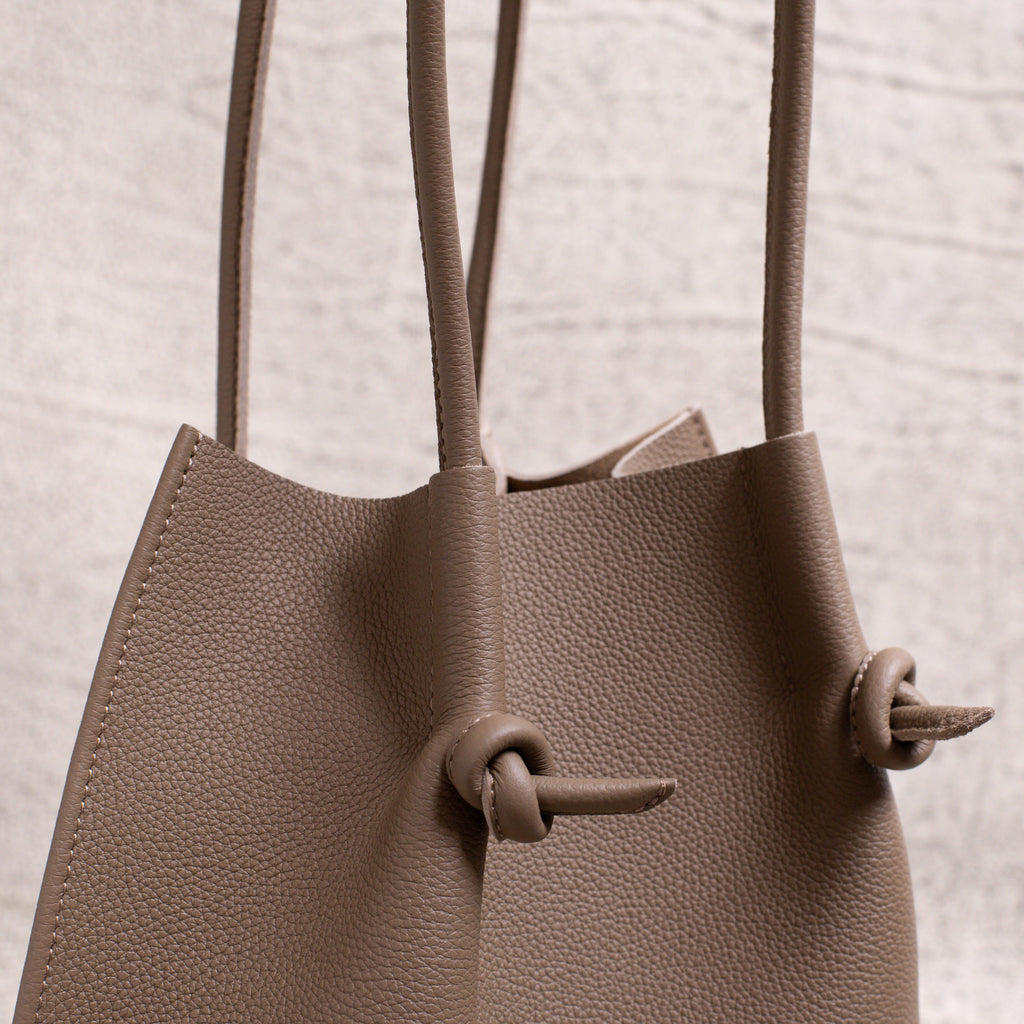 Side detail close-up showing the folded seam, dual handles, and signature knotted leather accents of the Etoupe edition.