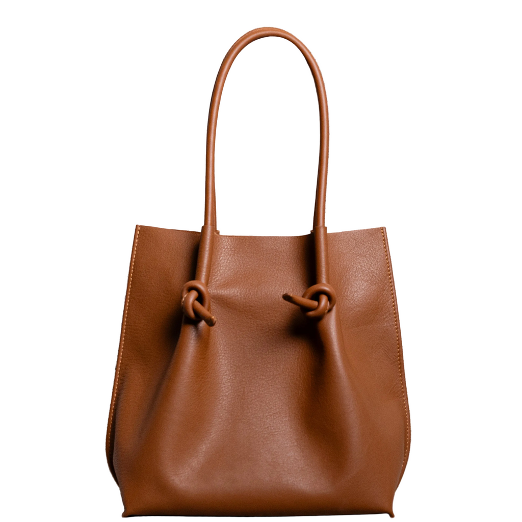 Flora Everyday Leather Tote in Urban Calf Taba, front view on white background. Structured bucket-style tote with tall rolled leather handles and two knotted leather ties cinching the open top.