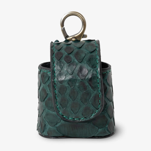Coil AirPods case in Jungle python leather, angled side view. Rich forest green scales with deep black undertones and natural texture variation. Curved magnetic closure with teal contrast stitching. Aged brass clip hardware.