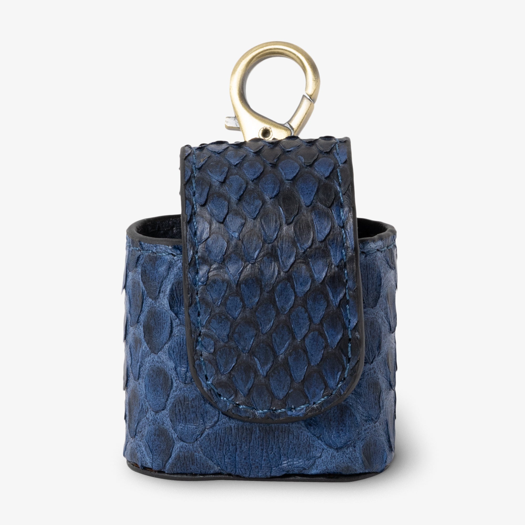 Coil AirPods case in Marine python leather, angled side view. Rich deep blue scales with subtle dark undertones and natural scale variation. Curved magnetic closure with black trim. Antique brass clip hardware.