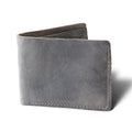 Bureau Leather Bifold Wallet in Rock Gray, standing upright at a three-quarter angle on a white surface. Dallas Crazy Horse calfskin in a cool slate gray tone with natural waxy surface variation, visible pull-up depth, and characteristic friction markings. Tonal gray saddle stitching runs along the right edge and bottom. Wallet slightly open, revealing a raw suede interior spine.