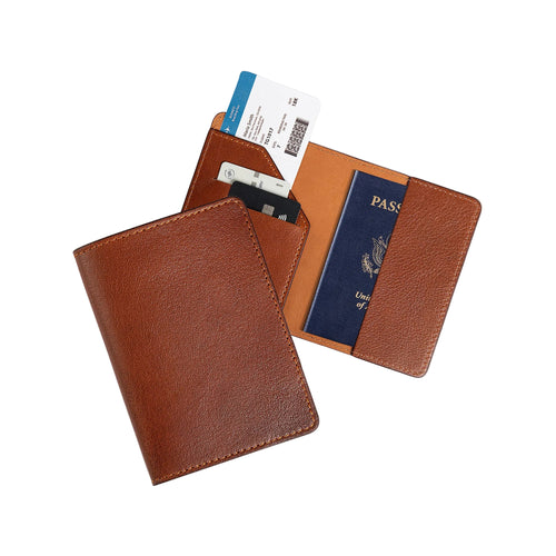 Two cognac brown leather passport wallets on gray: one closed showing the smooth fine-grain exterior, one open with diagonal card pocket holding two cards and a boarding pass on the left, and a U.S. passport inserted on the right. Warm amber tan lining and tonal brown stitching throughout.
