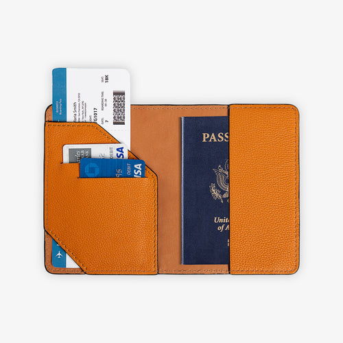 Full interior view of the open taba orange leather passport wallet, fully loaded. Left panel shows diagonal-cut orange card pocket with two debit cards and a boarding pass fanned above. Right holds a U.S. passport. Warm amber tan leather lining with tonal orange saddle stitching on all edges.