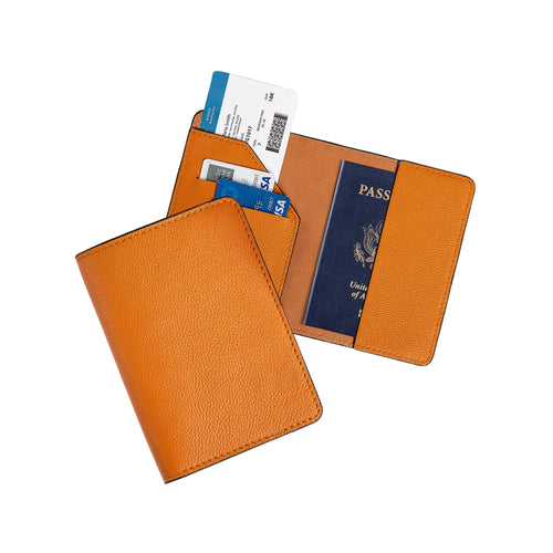 Two taba orange leather passport wallets on gray: one closed showing the vibrant pebbled exterior, one open with diagonal card pocket holding two debit cards and a boarding pass on the left, and a U.S. passport inserted on the right. Warm amber tan lining and tonal orange stitching throughout.