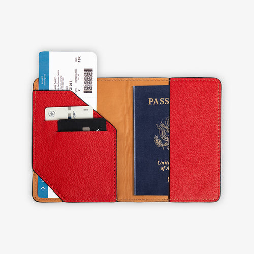 Full interior view of the open red leather passport wallet, fully loaded. Left panel shows diagonal-cut red card pocket with two cards and a boarding pass fanned out above. Right panel holds a U.S. passport. Warm cognac tan leather lining with tonal red saddle stitching on all edges.