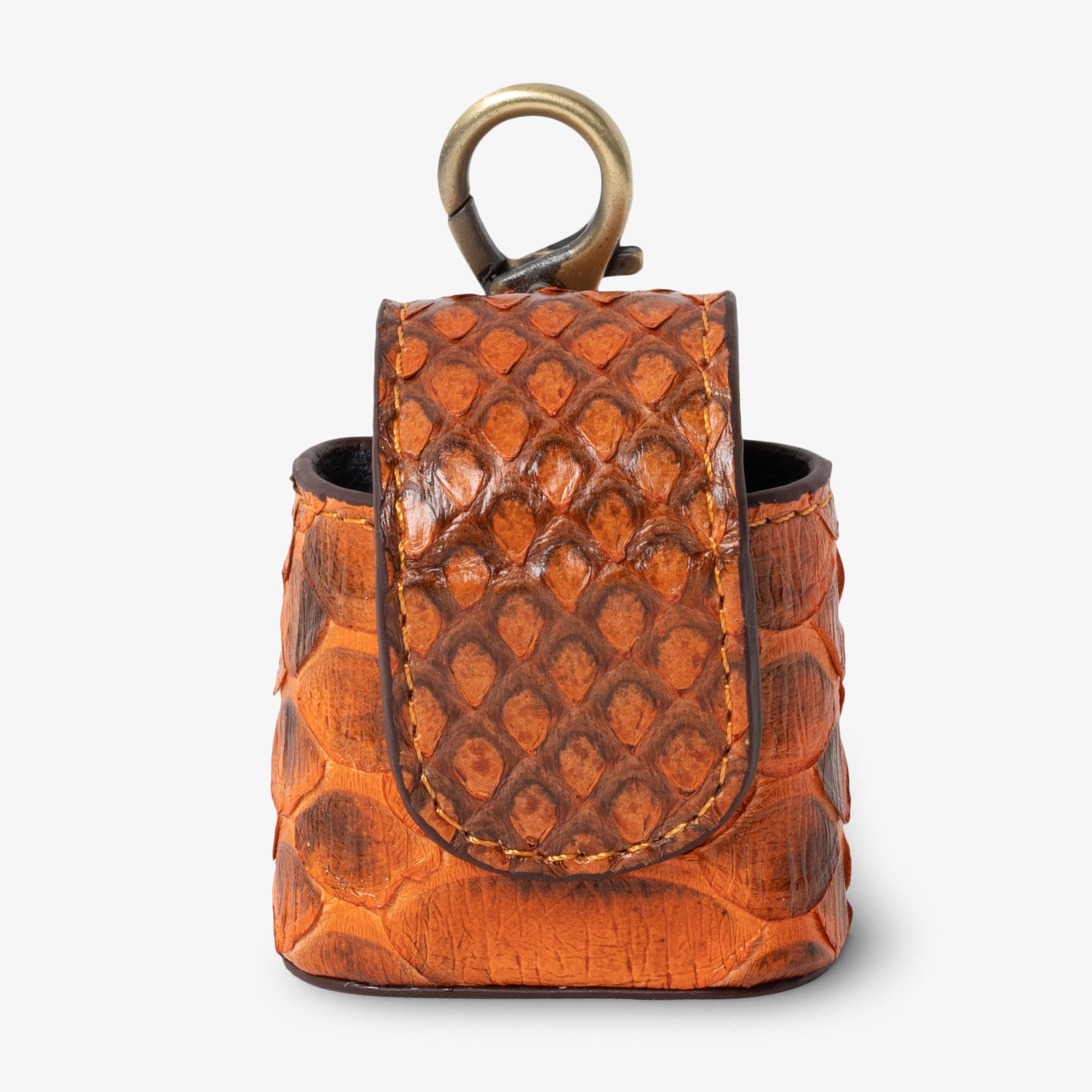 Coil AirPods case in Sunset python leather, angled side view. Vibrant orange and deep brown scales with golden contrast stitching detail. Curved magnetic closure with dark trim. Antique brass clip hardware.
