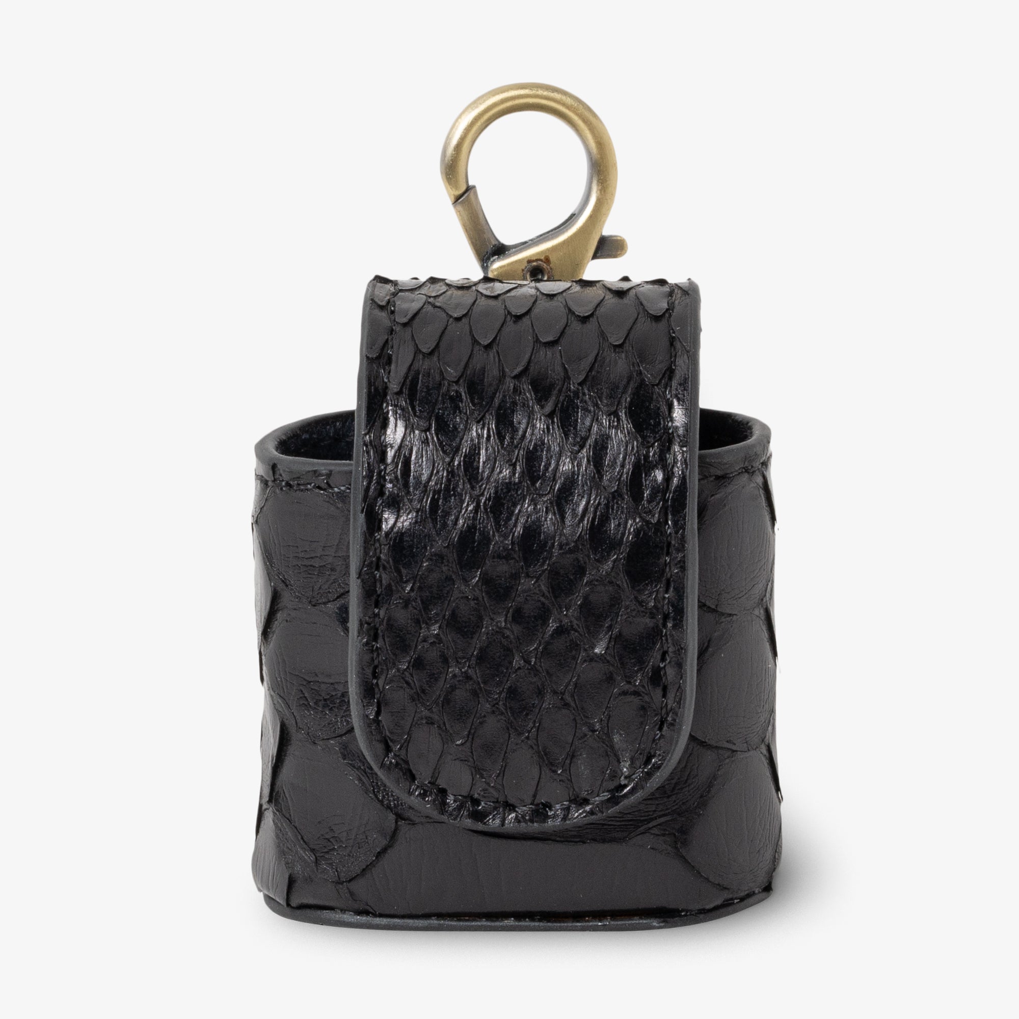 Coil AirPods case in Venom python leather, angled side view. Deep black scales with high-contrast gloss finish on flap against matte body. Curved magnetic closure with black trim. Antique brass clip hardware.