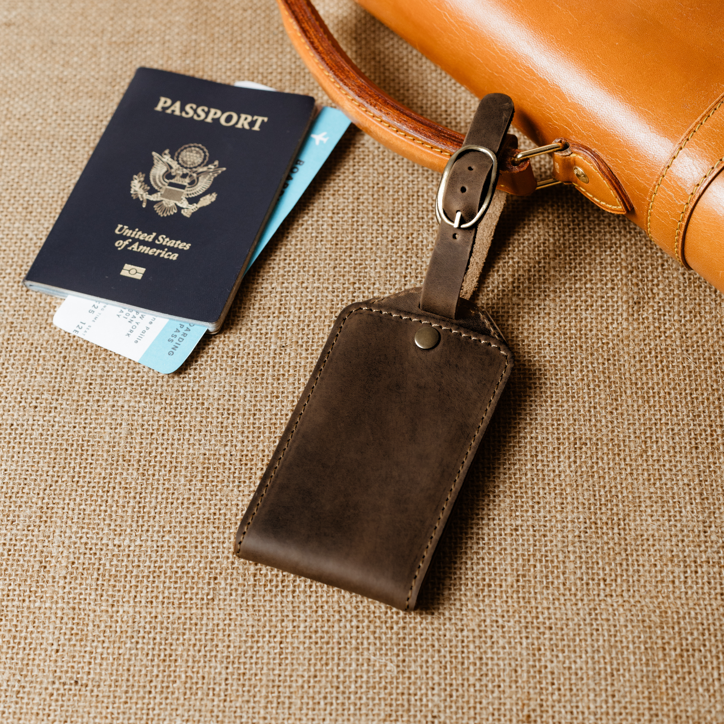 Brown leather luggage tag attached to a tan duffel, paired with a passport and tickets for stylish, ready-to-go travel.