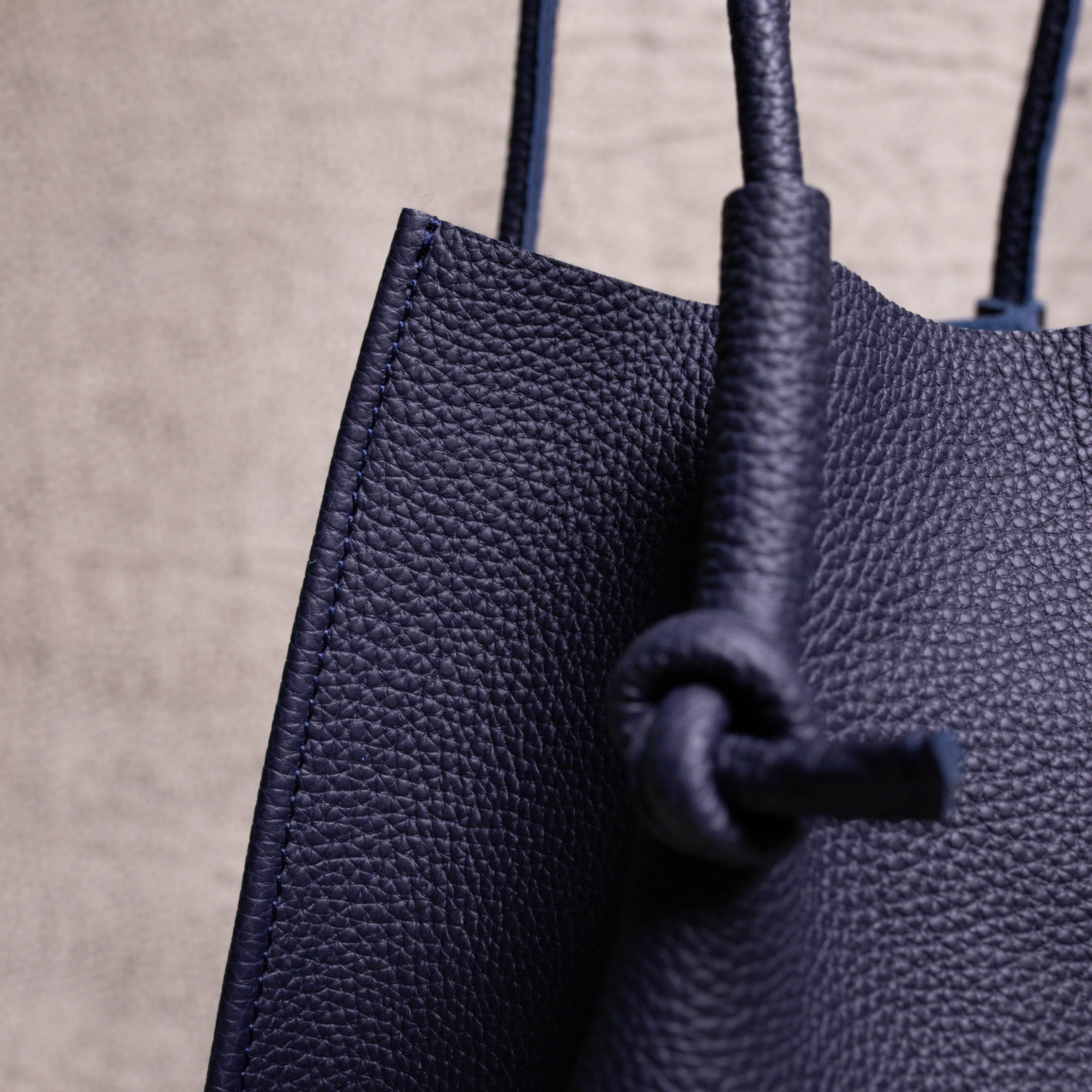 Close-up detail of the Flora Tote’s knotted handle and folded-edge stitching, showcasing the rich pebbled Togo leather and expert craftsmanship.