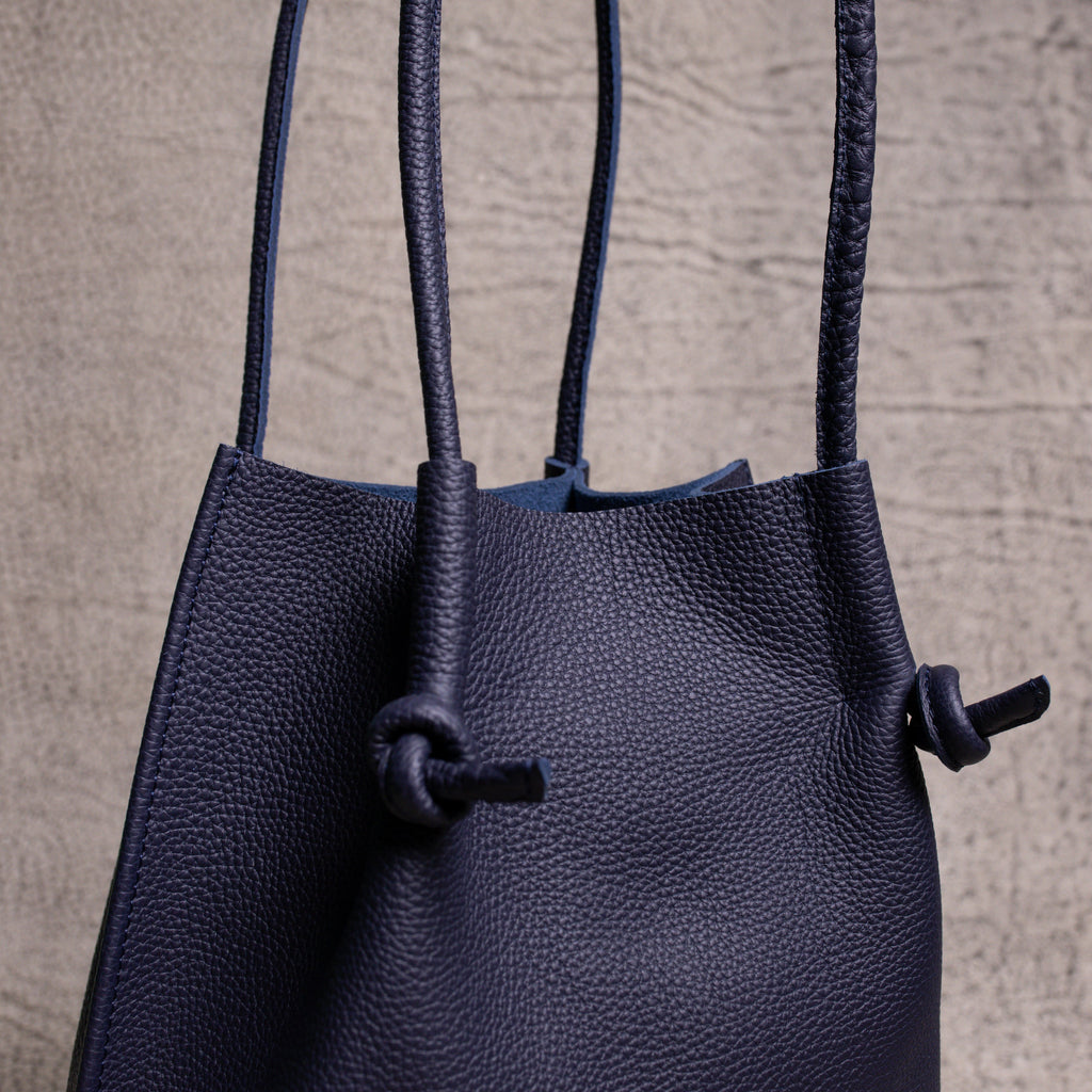 Side view of the Flora Tote in Togo Blue, highlighting its elegant drape, rolled handles, and natural movement of premium grained leather.