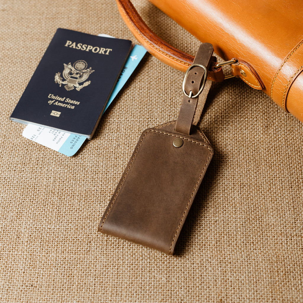 Brown leather luggage tag attached to leather bag beside passport and boarding pass