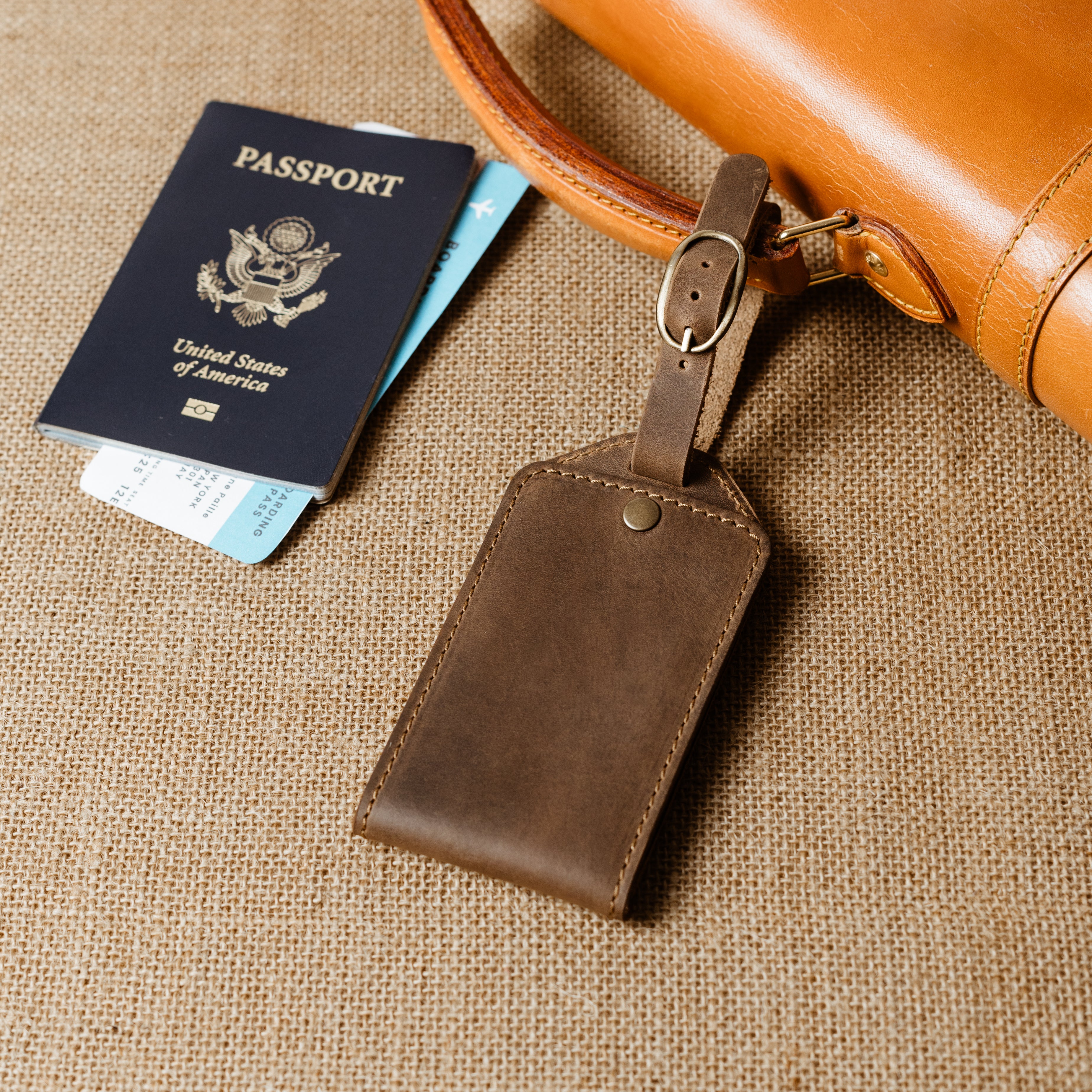 Brown leather luggage tag attached to leather bag beside passport and boarding pass