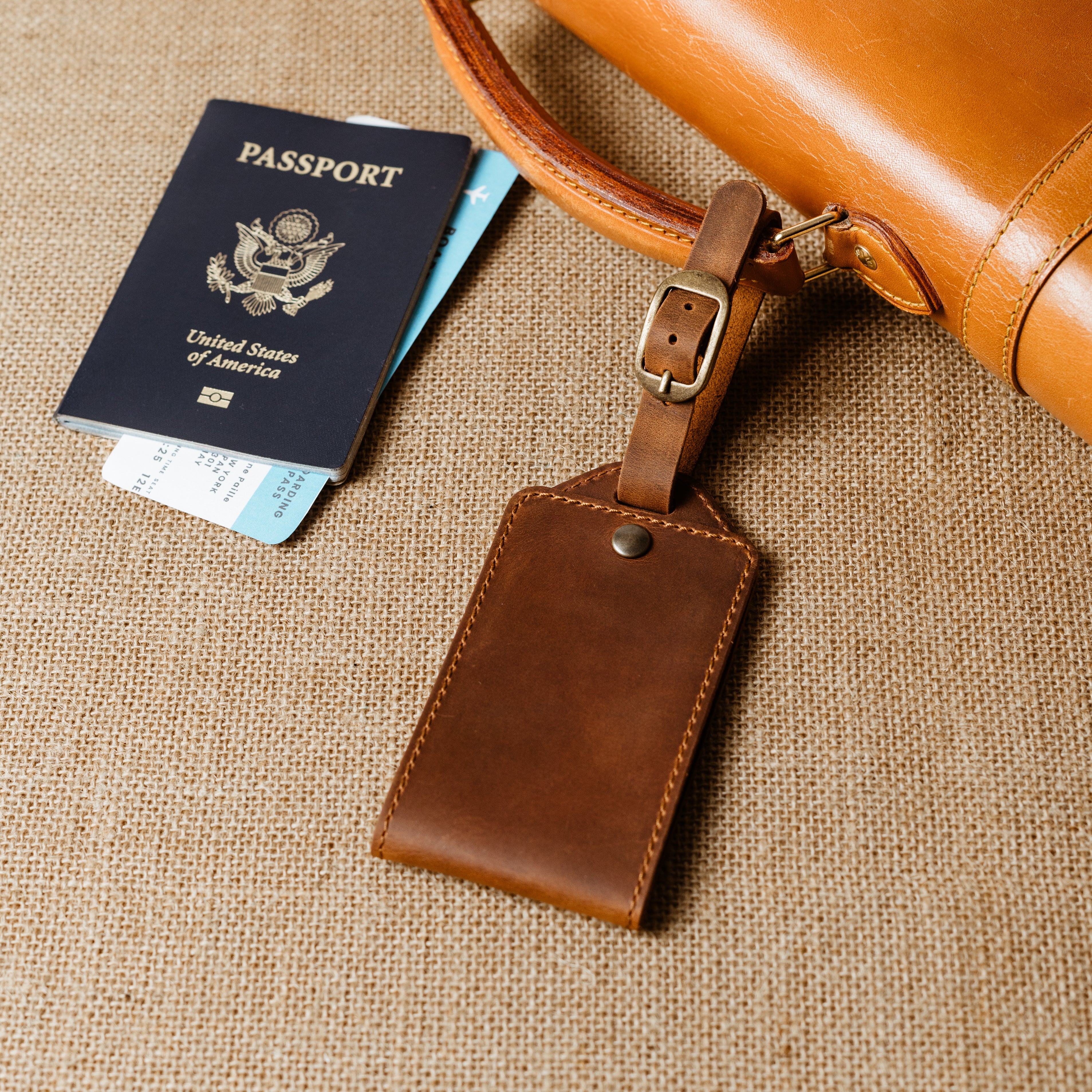 Handcrafted brown leather luggage tag attached to travel bag beside passport and boarding pass