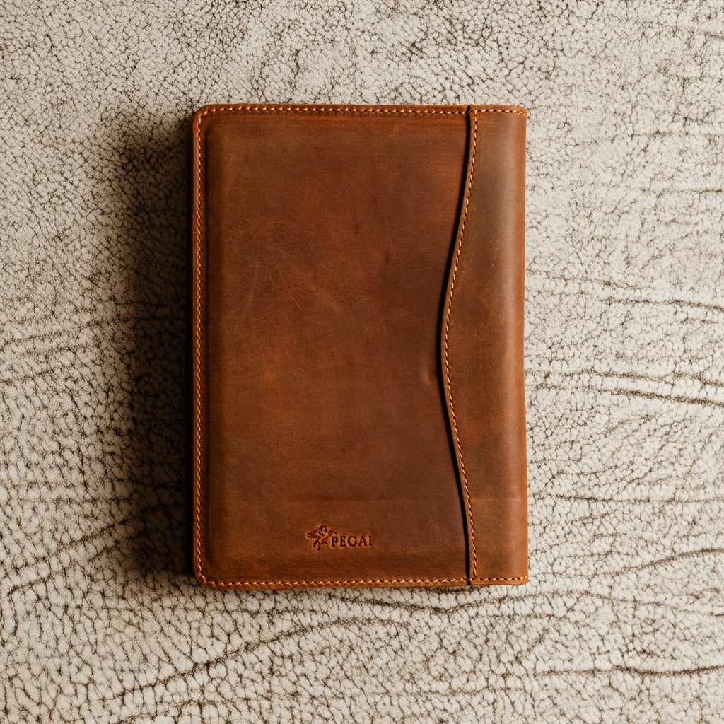 PEGAI Eriksen Jr. padfolio in mahogany Dallas Crazy Horse leather lying closed on a textured white surface, showing PEGAI pegasus logo and curved seam stitching. 