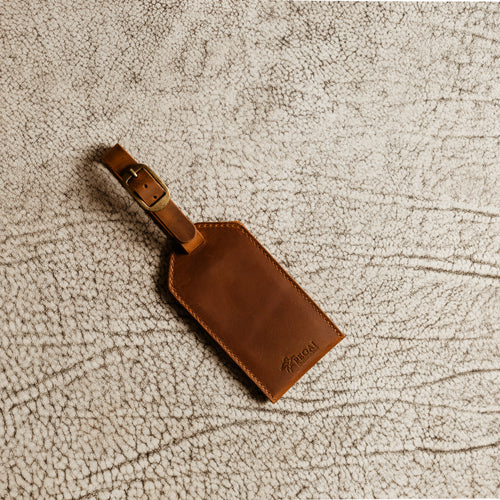Brown Dallas Crazy Horse leather luggage tag with antique brass buckle on textured neutral background
