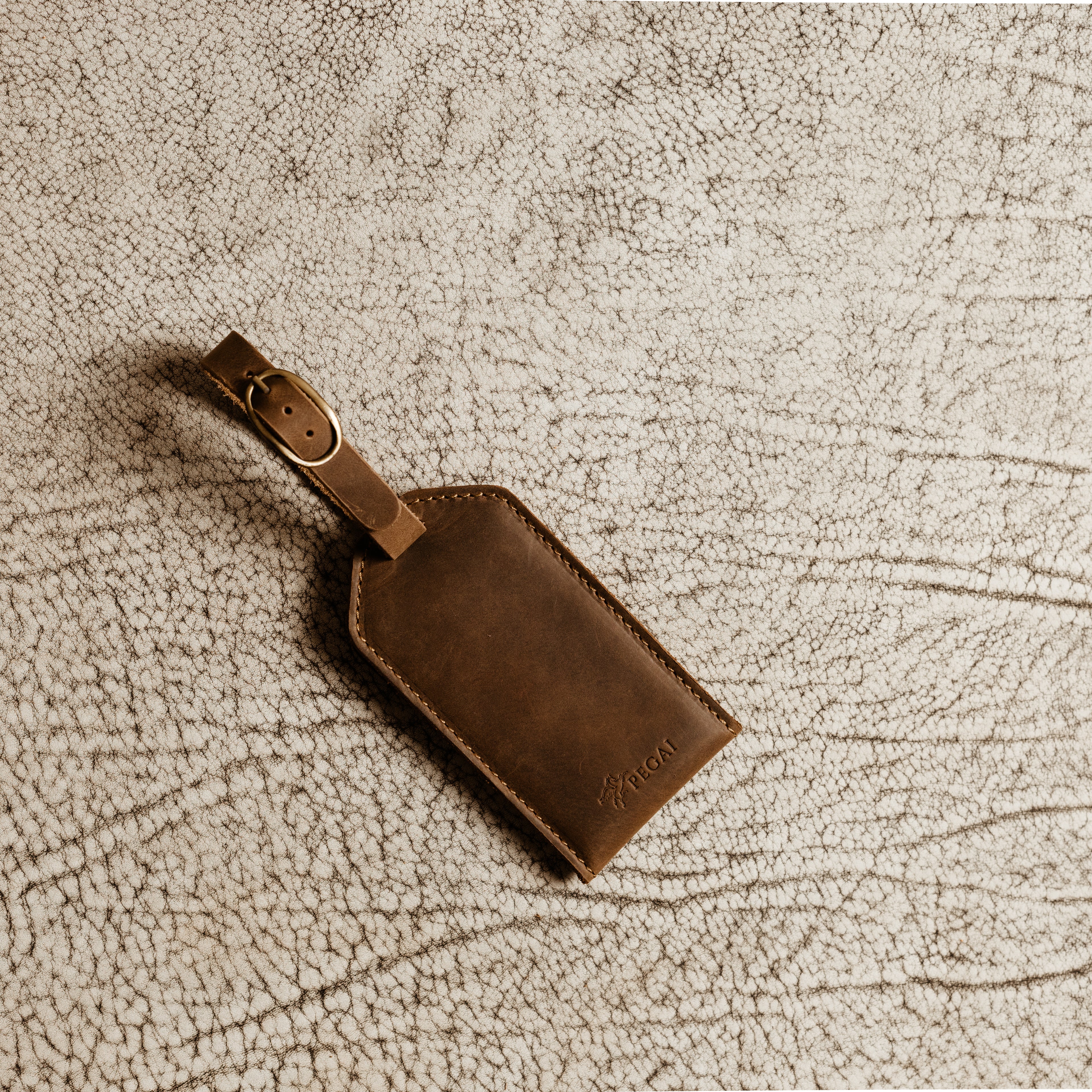 Brown leather luggage tag with antique brass buckle resting on textured leather surface