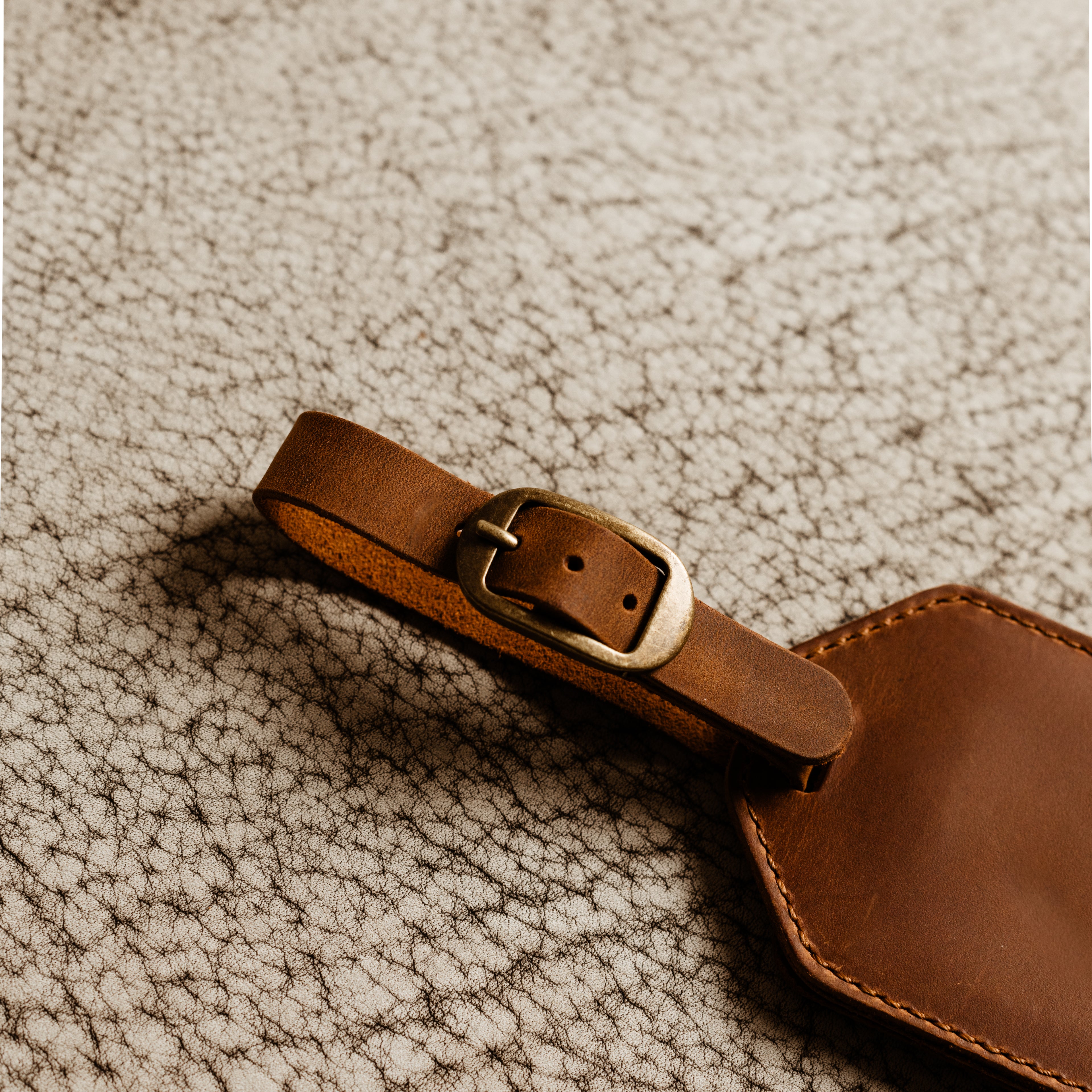 Close-up of antique brass buckle and brown Crazy Horse leather luggage tag strap