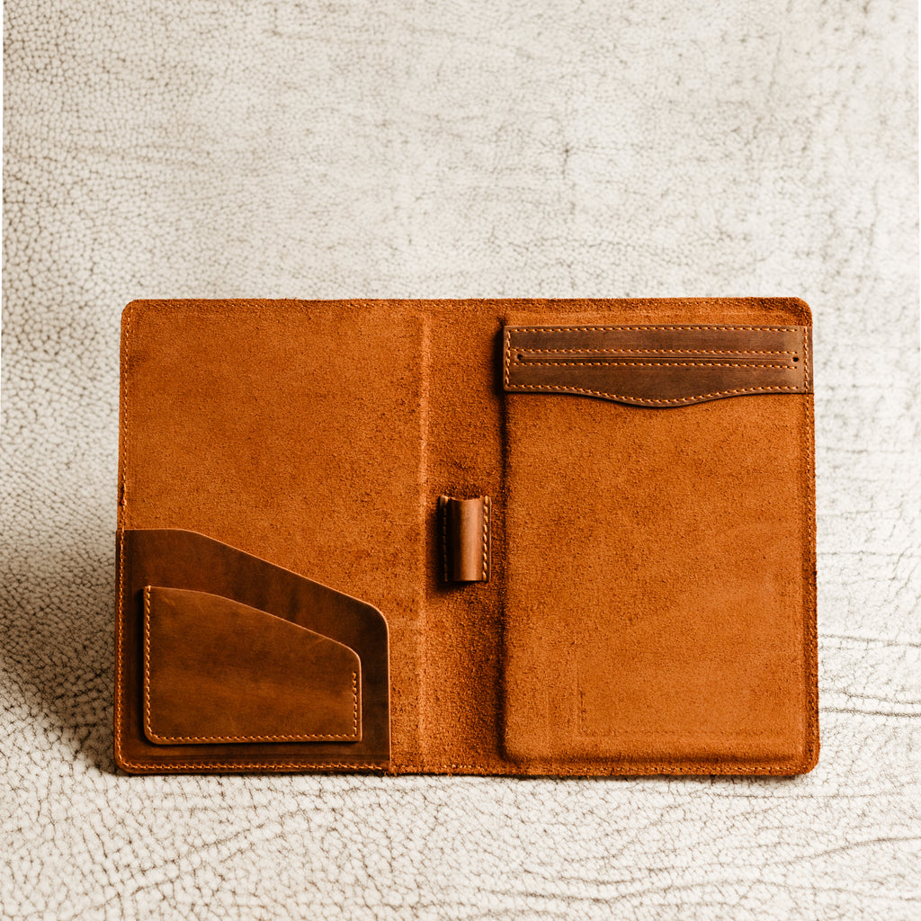 PEGAI Eriksen Jr. padfolio open and empty on a textured white surface, showing warm tan suede lining, card slot, pen loop, and business card pocket in mahogany leather. 