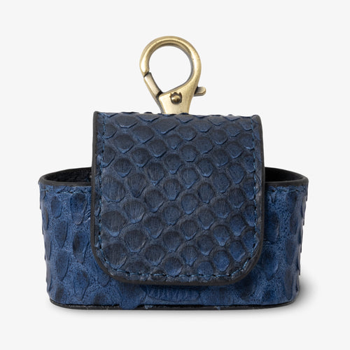 Coil AirPods case in Marine python leather, front view. Deep navy and midnight blue scales with natural texture variation. Magnetic flap closure and antique brass keychain clip at top. Black interior visible.