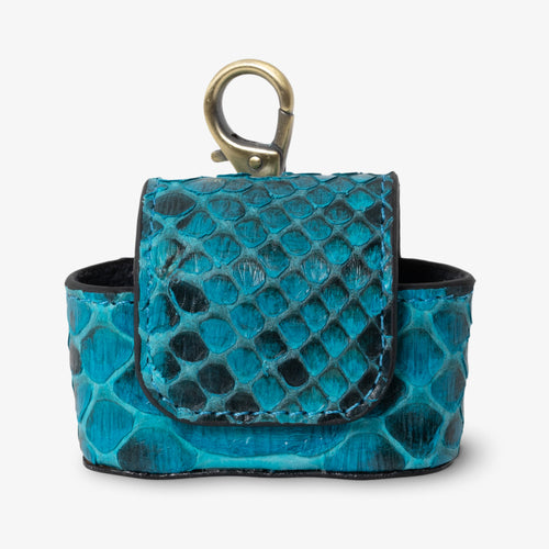 Coil AirPods case in Sky python leather, front view. Vivid teal and deep black scales with natural variation. Magnetic flap closure and antique brass keychain clip at top. Black suede interior visible.
