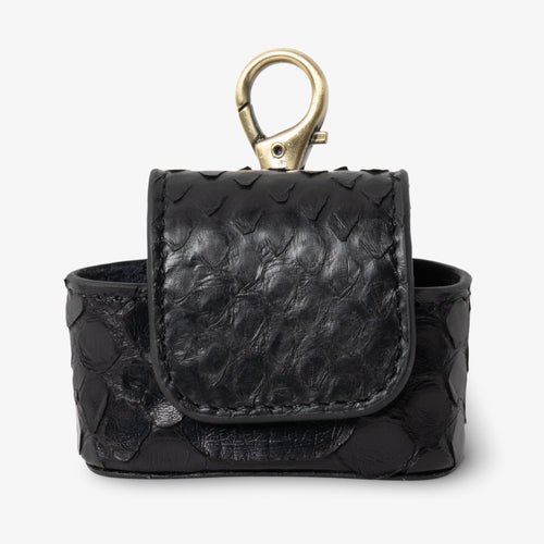 Coil AirPods case in Venom python leather, front view. Matte black scales with subtle organic texture variation and natural shine. Magnetic flap closure and antique brass keychain clip at top.